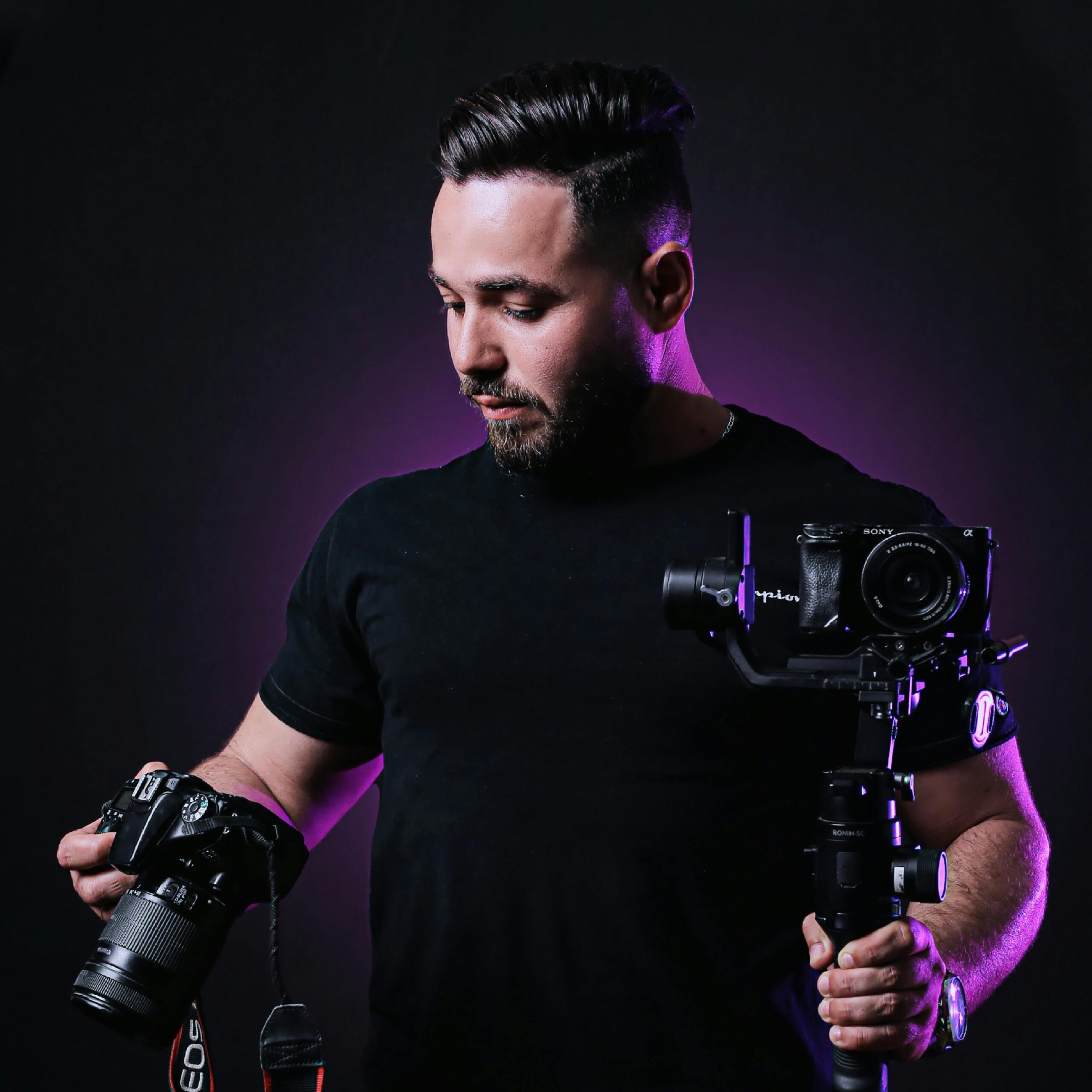 Portrait of a professional photographer holding cameras in a studio with purple ambient lighting.